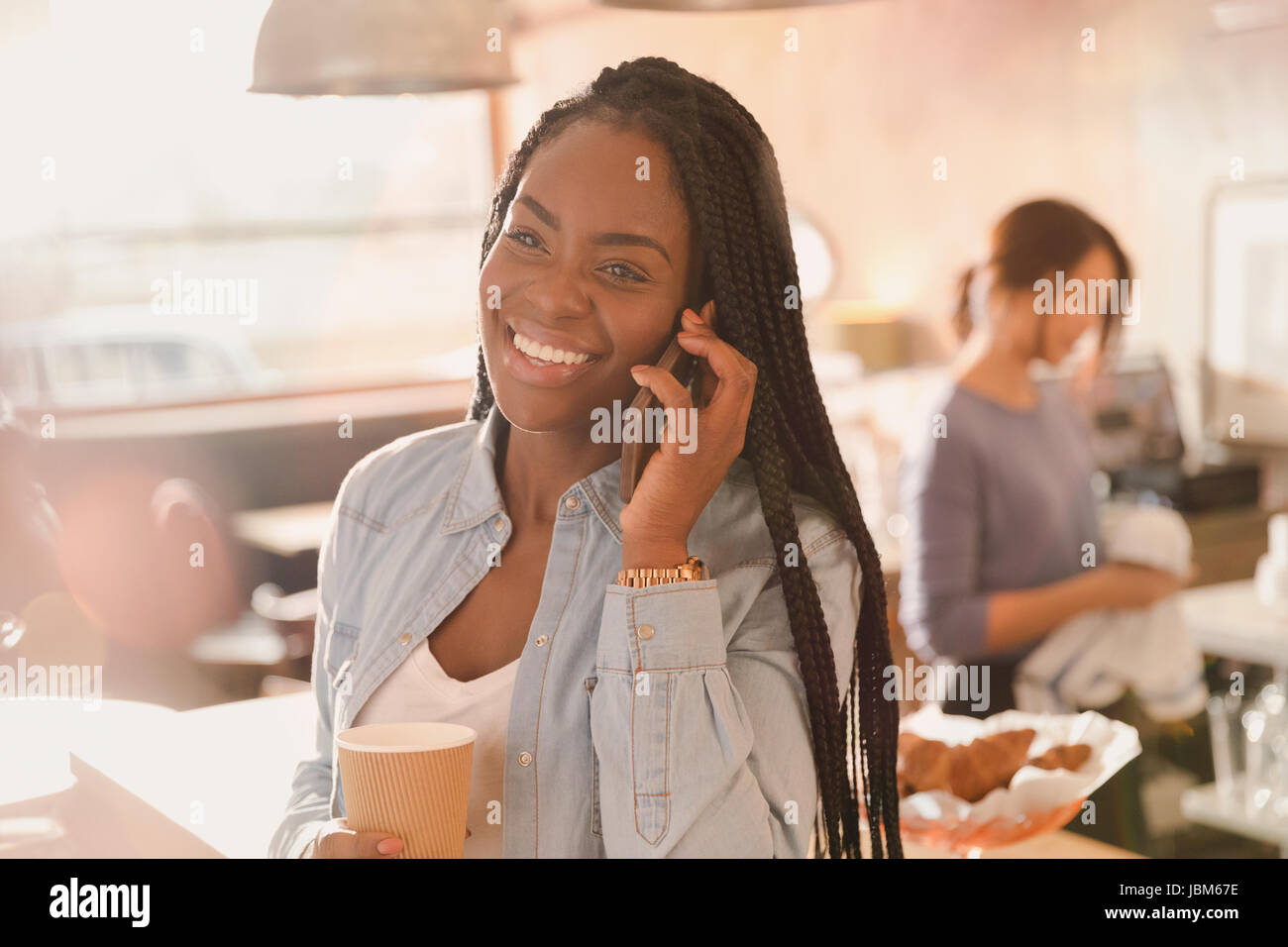 Smiling woman talking on cell phone and drinking coffee in cafe Stock Photo