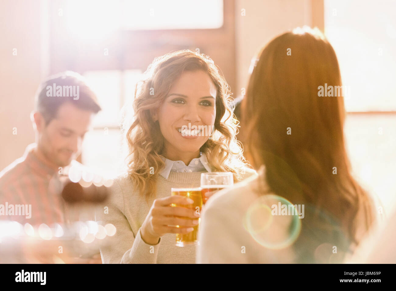 Smiling women friends toasting beer glasses in sunny bar Stock Photo
