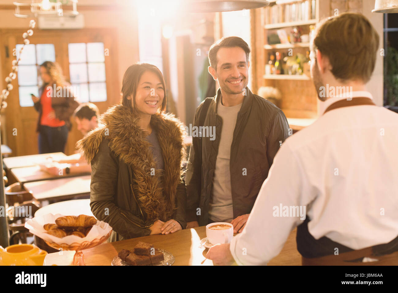 Barista serving coffee to couple at counter in cafe Stock Photo