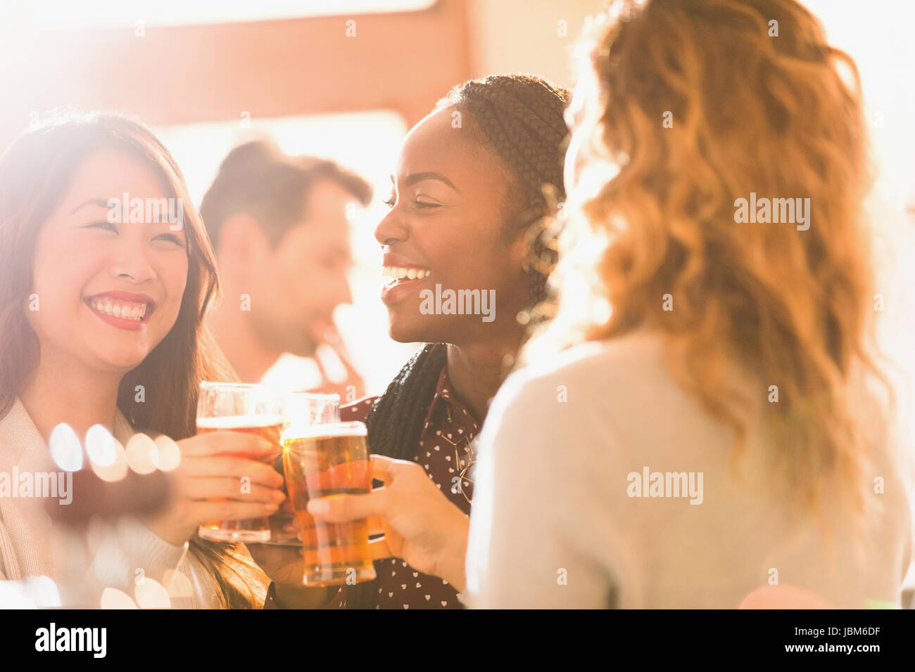 Smiling women friends toasting beer glasses in bar Stock Photo