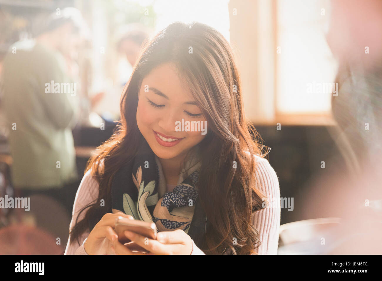 Smiling Chinese woman texting with cell phone in cafe Stock Photo