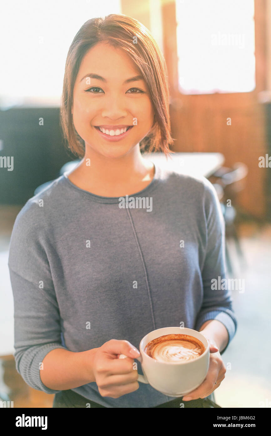 Portrait smiling Chinese woman drinking cappuccino in cafe Stock Photo