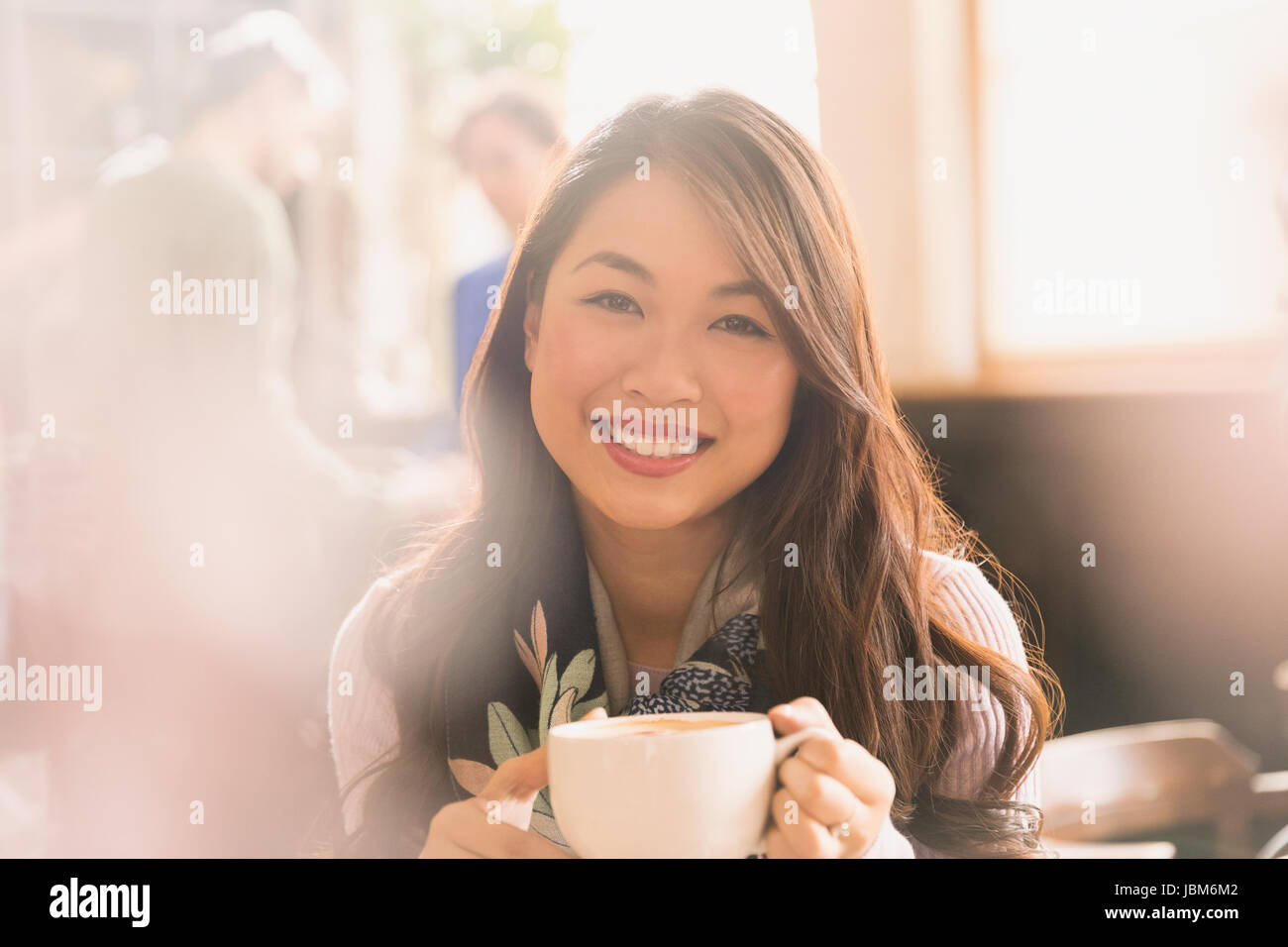 Portrait smiling Chinese woman drinking cappuccino in cafe Stock Photo