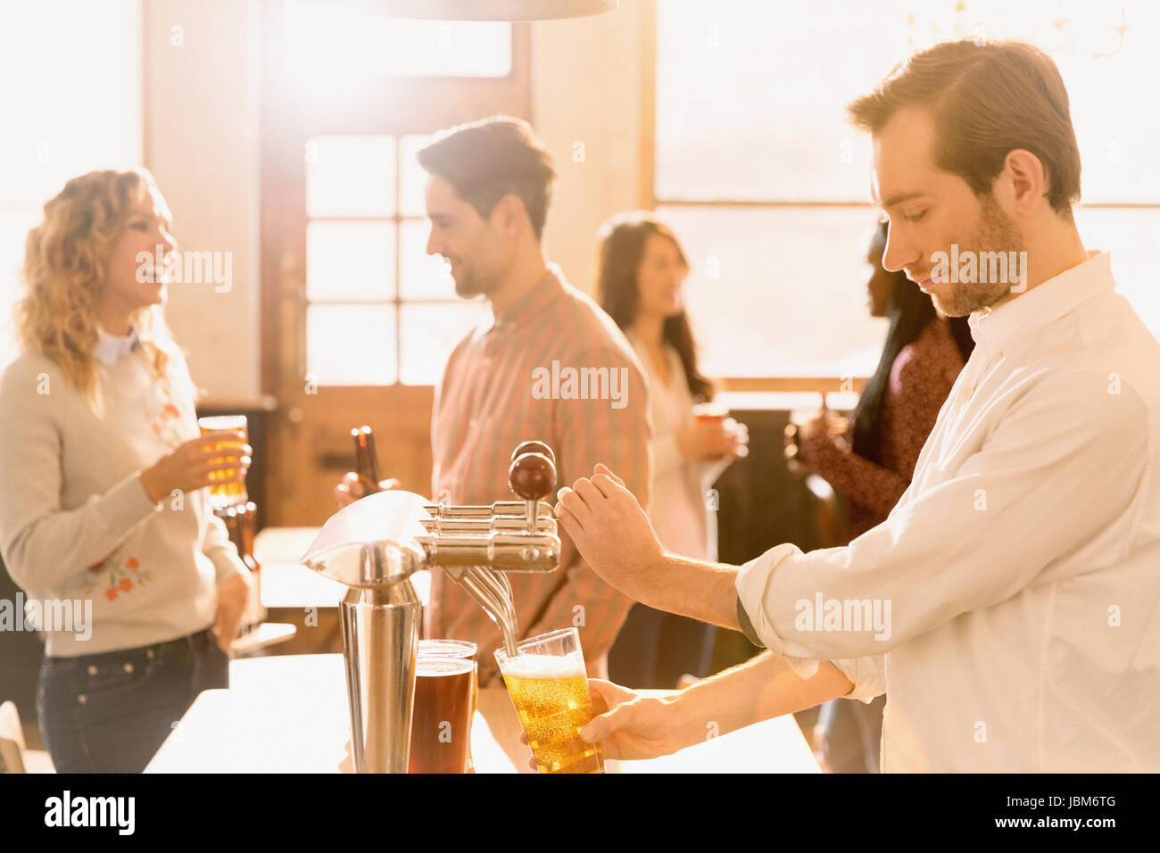 Bartender pouring beer at beer tap behind bar Stock Photo