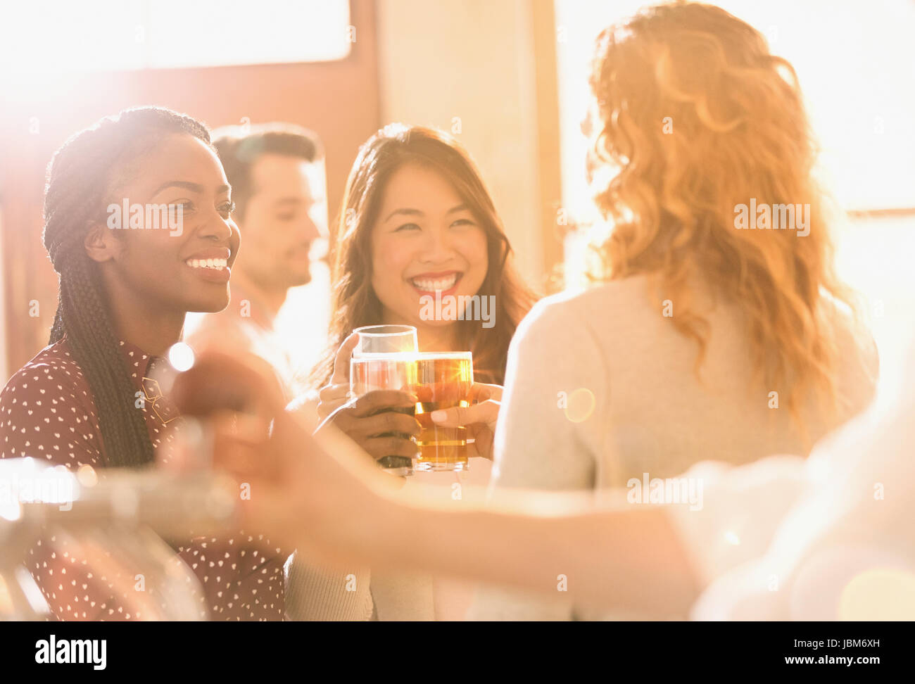 Smiling women friends toasting beer glasses in sunny bar Stock Photo