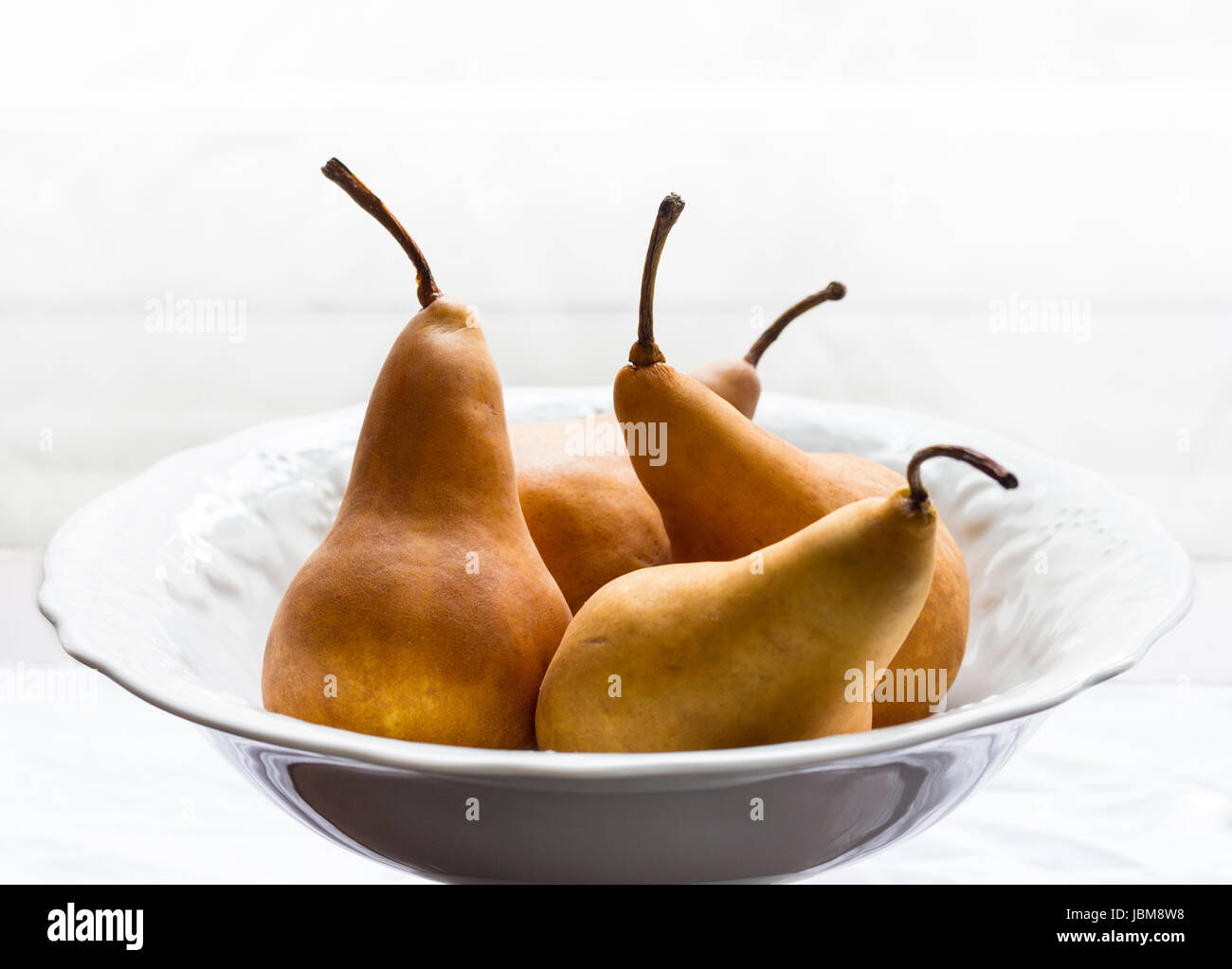 Golden pears in white porcelain bowl. High key lighting. Horizontal format. Stock Photo