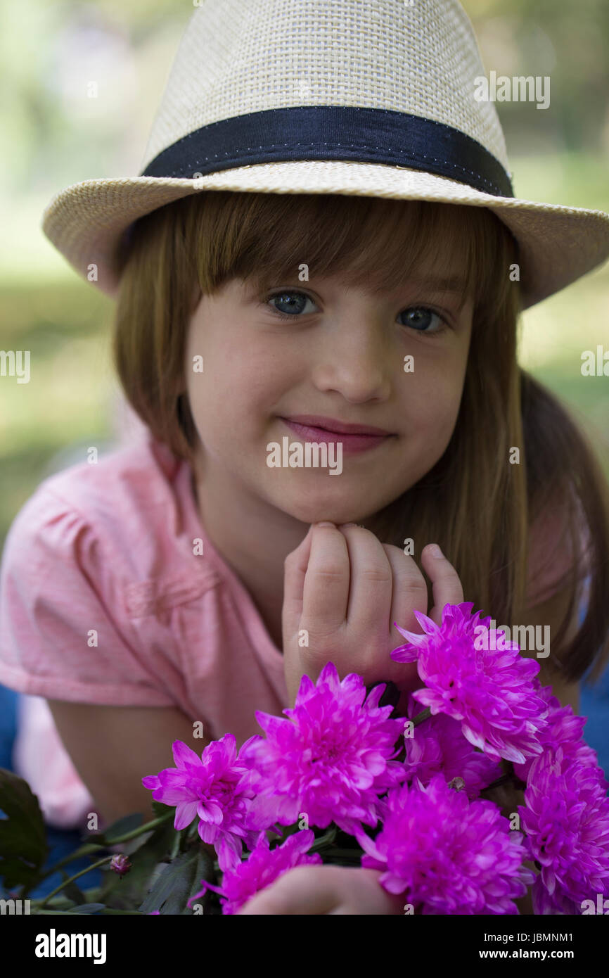 Little cute girl in a hat holding a bouquet of flowers and enjoy nature ...