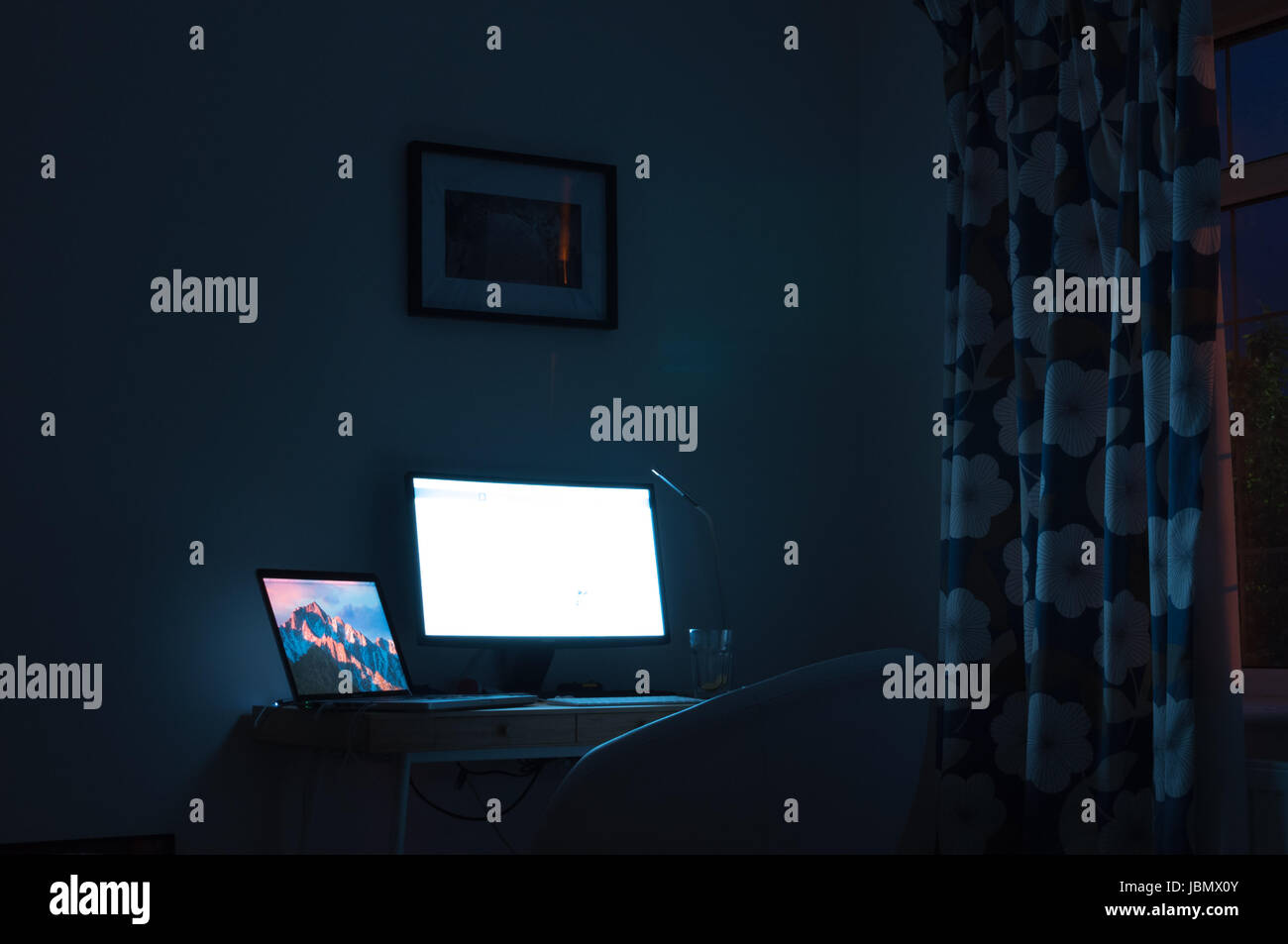 Computer screen illuminating a dark room at night Stock Photo