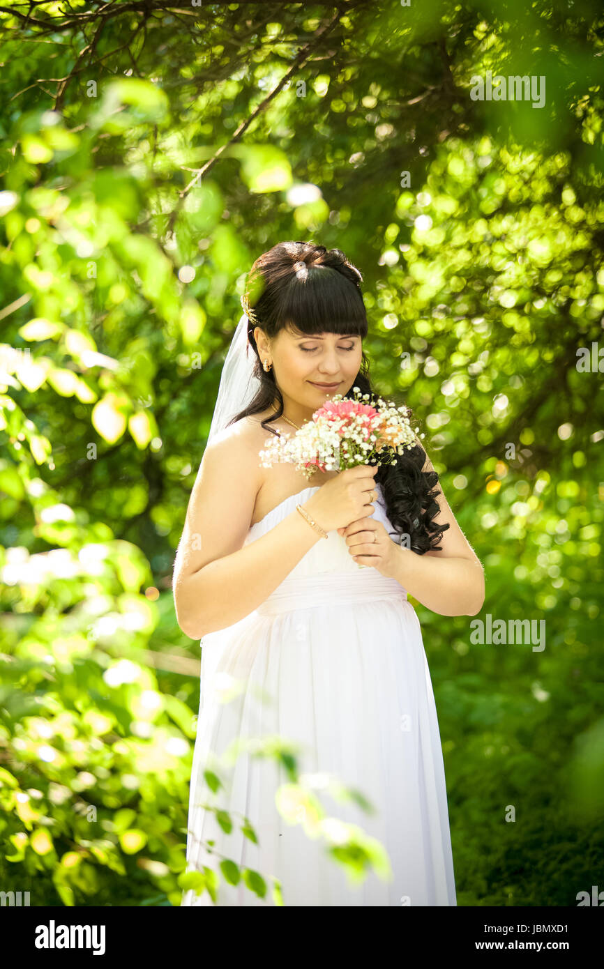 Portrait of smiling cute bride smelling bouquet at park Stock Photo - Alamy
