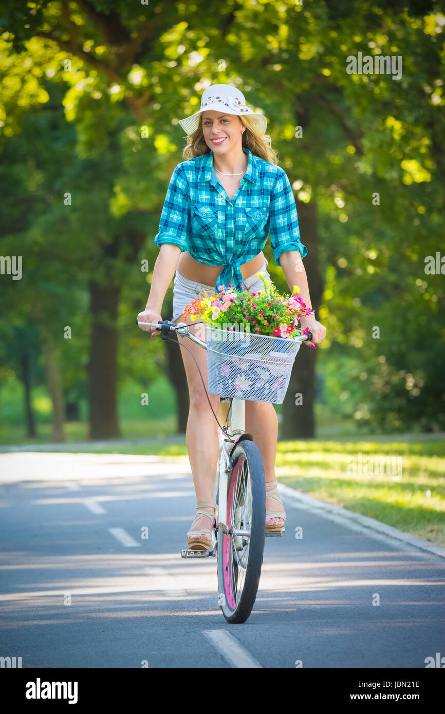 Pretty woman riding bicycle with basket full of flowers in a park. Active people vacation and lifestyle concepts Stock Photo Alamy