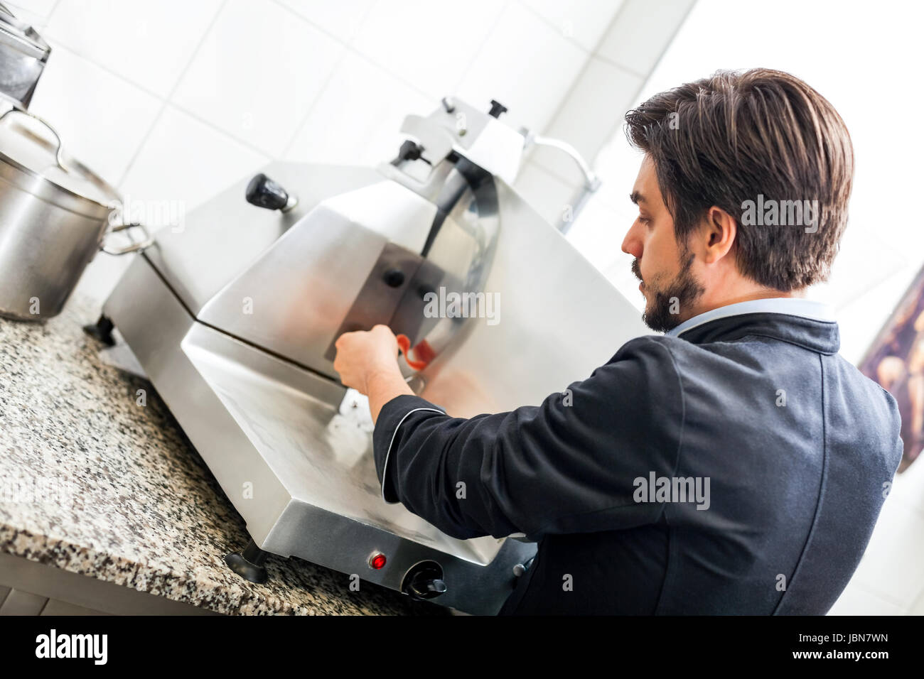 chefkoch schneidet frischen schinken auf der schneidemaschine in der restaurant küche Stock Photo