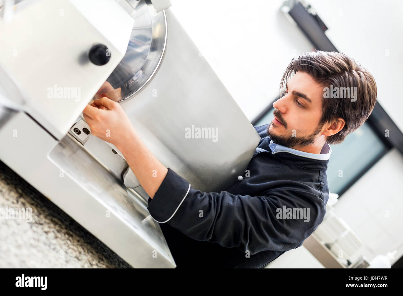 chefkoch schneidet frischen schinken auf der schneidemaschine in der restaurant küche Stock Photo