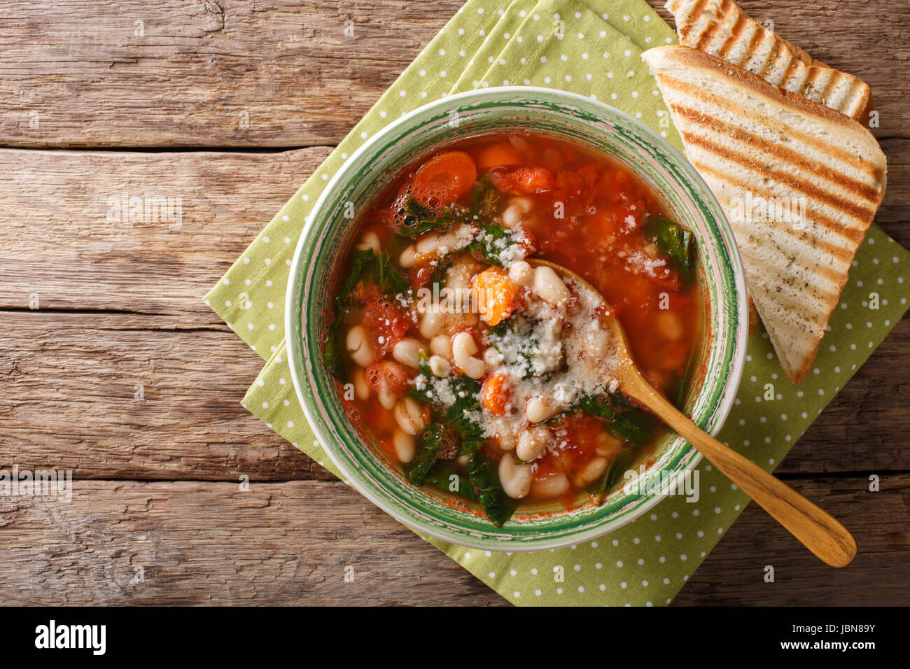Tomato soup with beans, spinach and parmesan close-up on the table. horizontal view from above Stock Photo