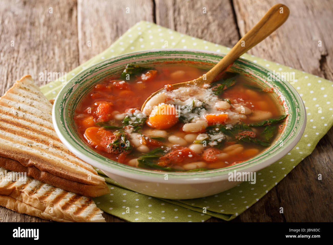 Tomato soup with beans, spinach and parmesan close-up on the table. Horizontal Stock Photo