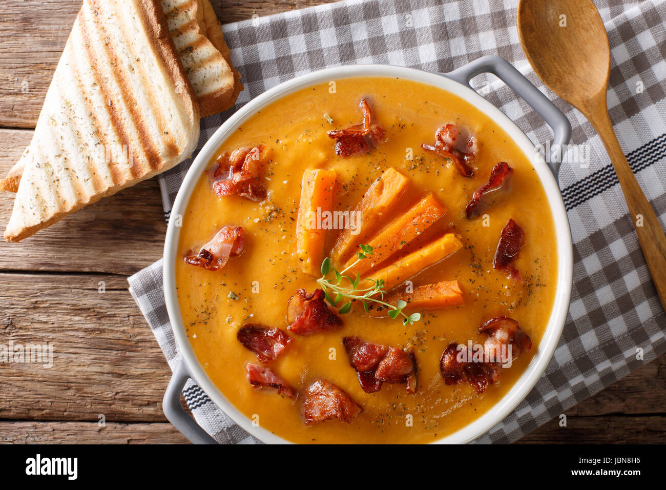 Soup of sweet potato with bacon and herbs in a saucepan and toast close-up on a table. horizontal view from above Stock Photo
