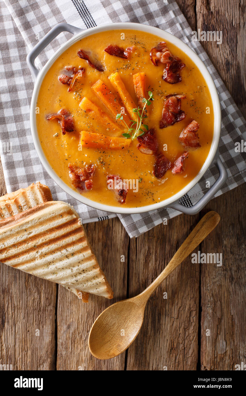 Soup of sweet potato with bacon and herbs in a saucepan and toast close-up on a table. Vertical view from above Stock Photo