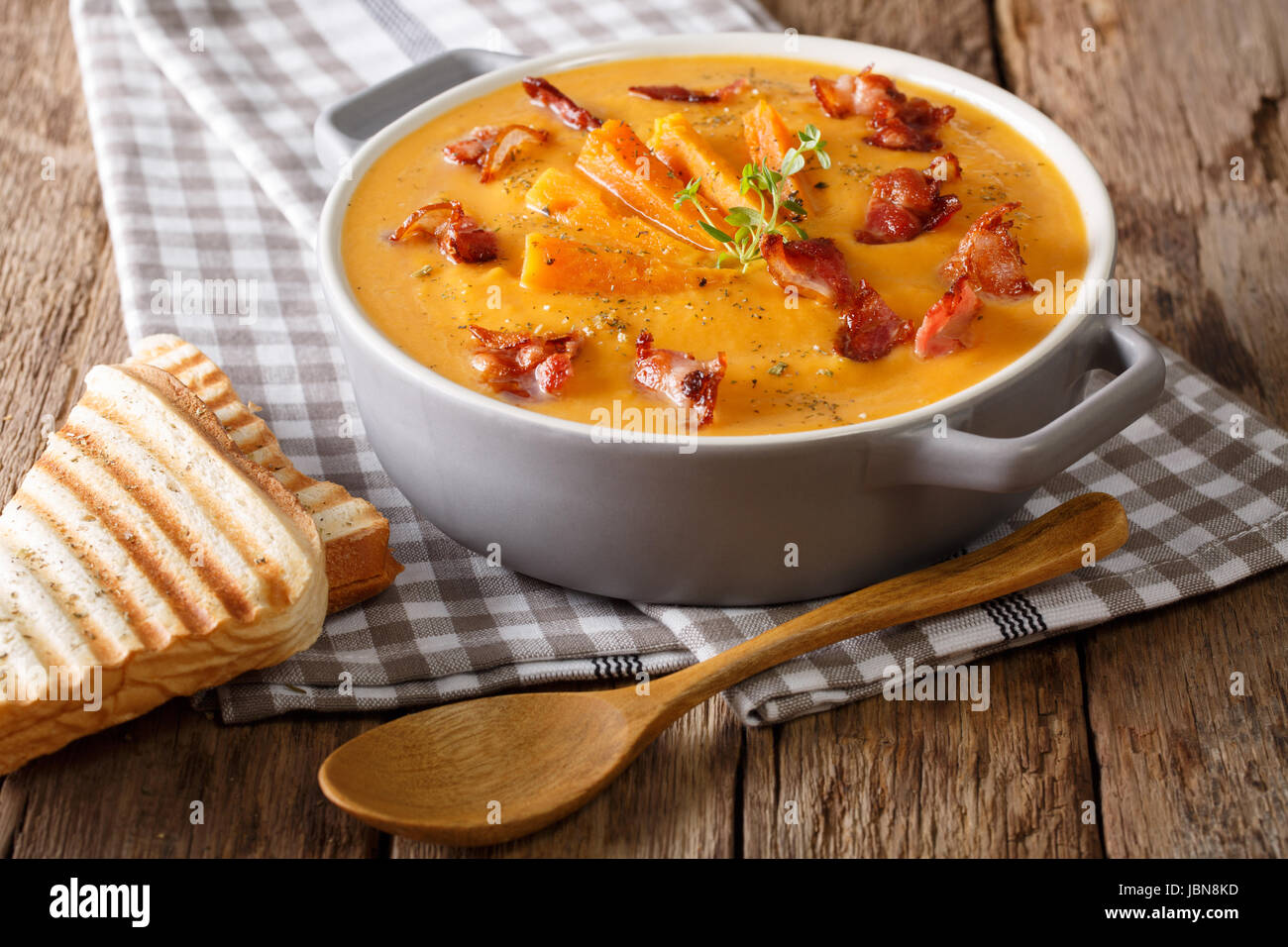 Sweet potato soup with bacon and herbs in a pan and toast close-up on the table. horizontal Stock Photo