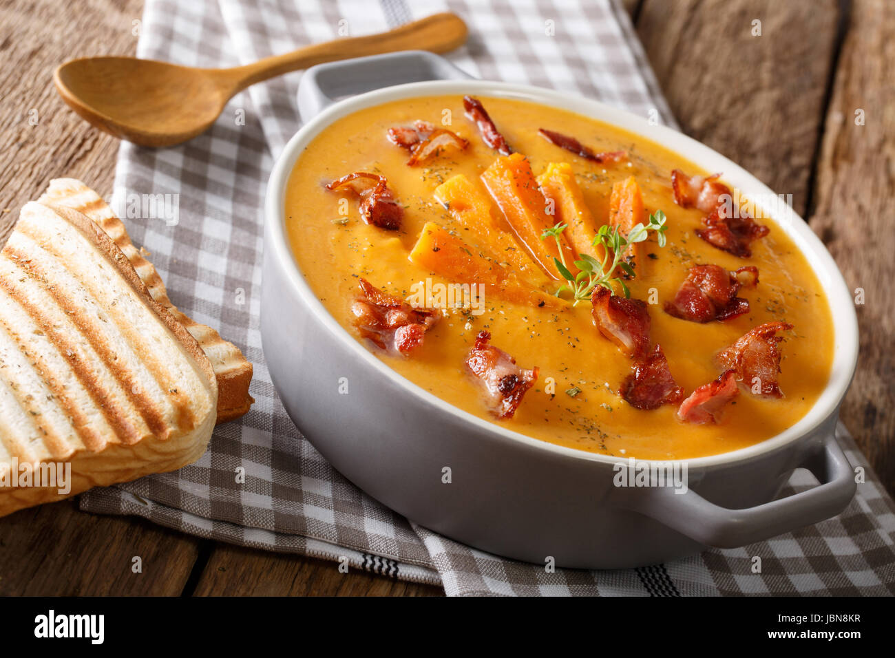 Healthy sweet potato cream soup with bacon and herbs in a saucepan and toast closeup on a table. horizontal Stock Photo