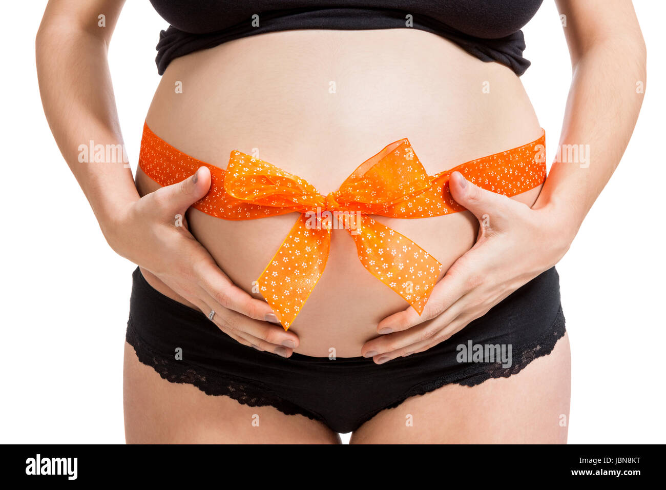Junge schwangere Frau mit orangener Schleife um den Bauch als Nahaufnahme isoliert vor weißem Hintergrund Stock Photo