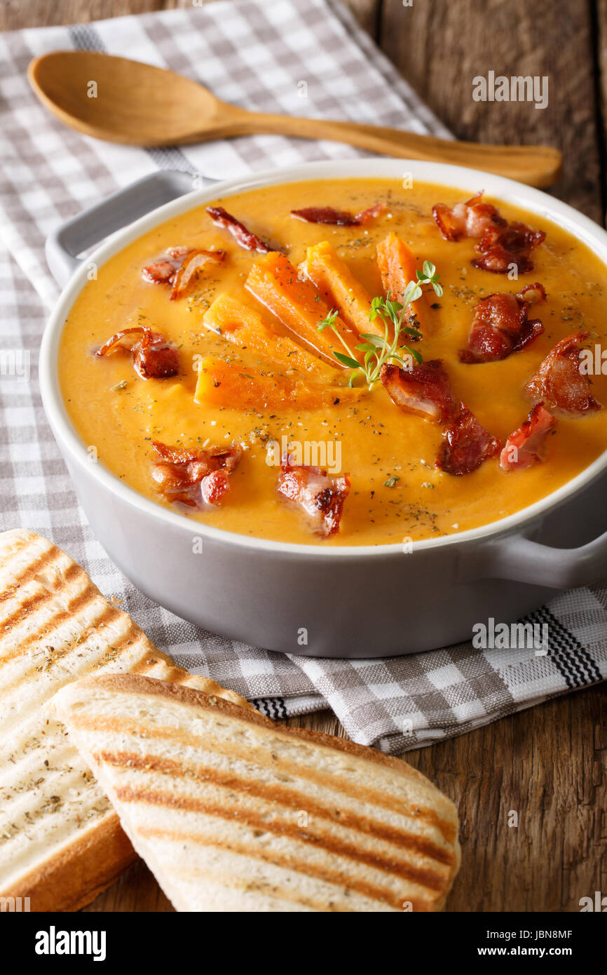 Healthy sweet potato cream soup with bacon and herbs in a saucepan and toast closeup on a table. Vertical Stock Photo