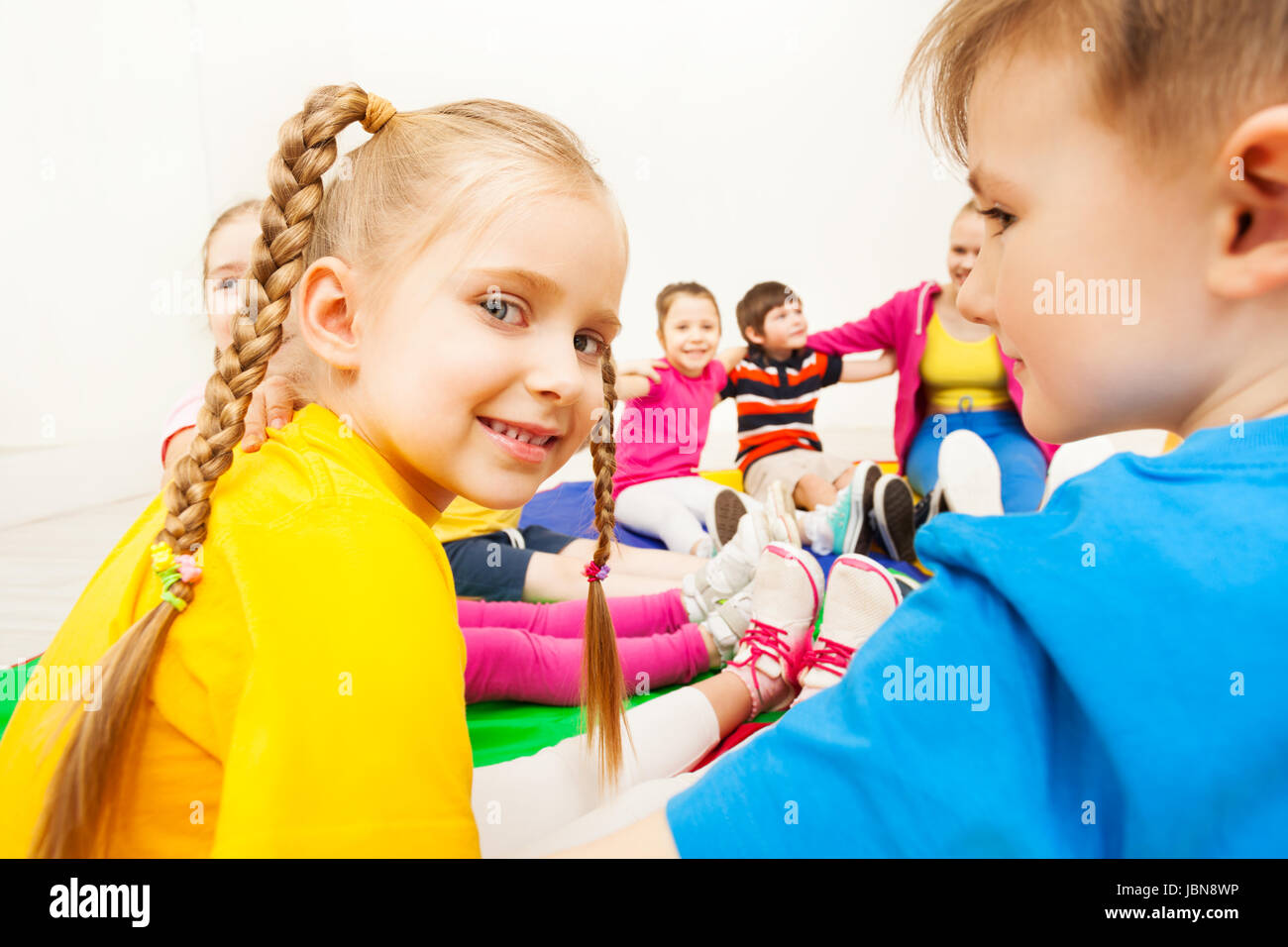 Close-up portrait of blond six years old girl sitting in a circle with friends at school gym Stock Photo