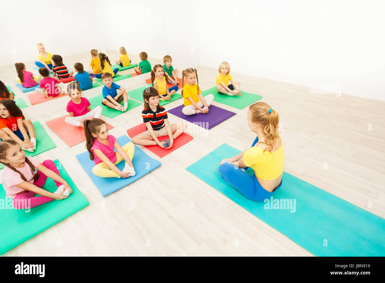 Group of sporty kids sitting on yoga mats and doing butterfly stretch with female instructor in exercise room Stock Photo