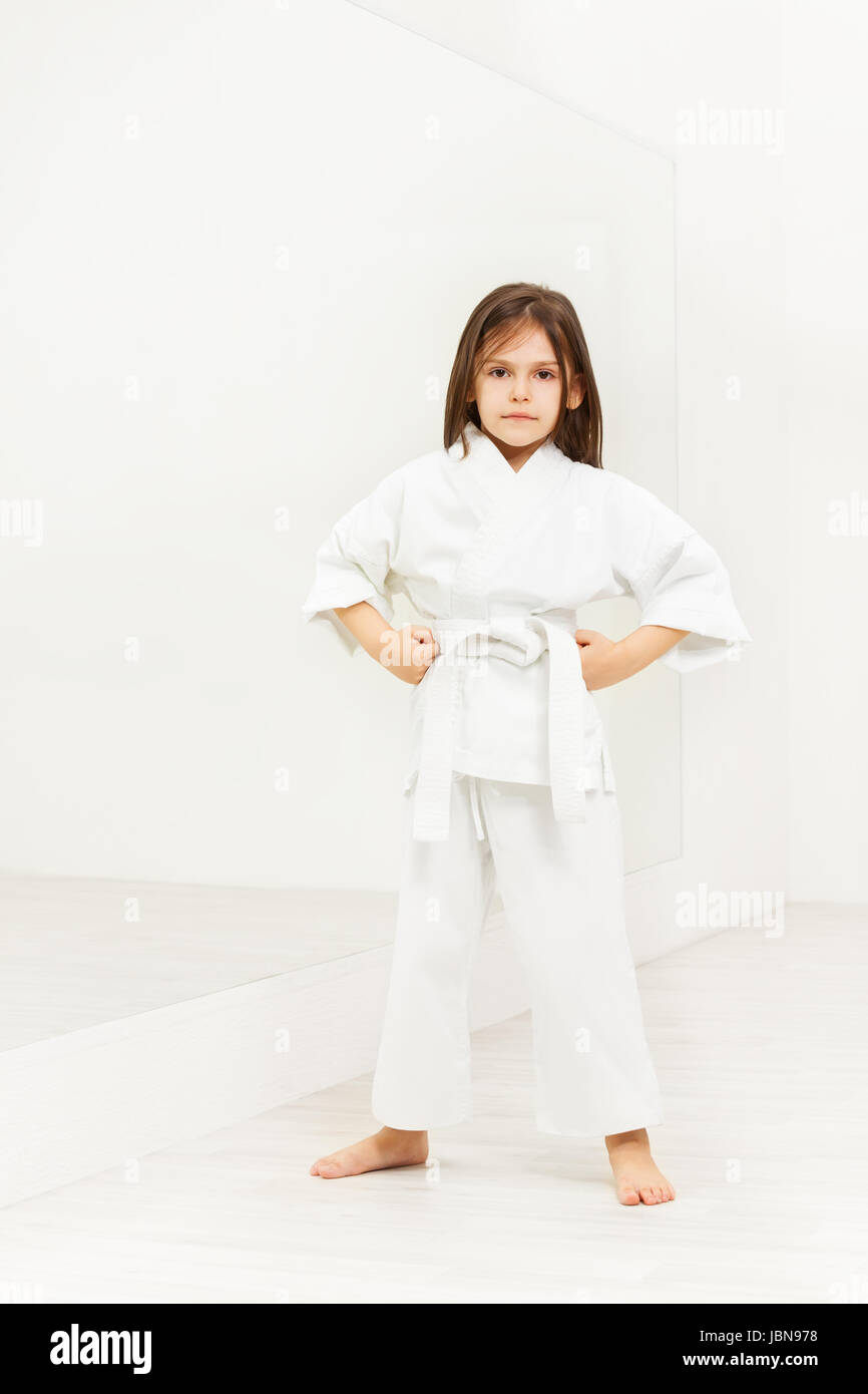 Full length portrait of karate girl in white kimono standing with hands on hips in light gym Stock Photo