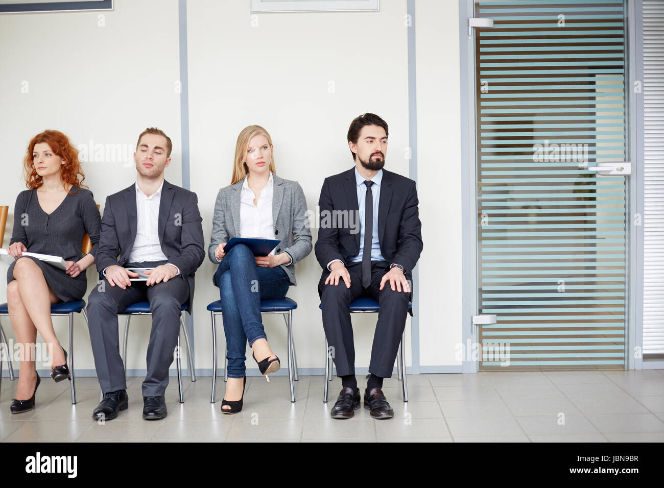 Portrait of several business associates sitting on chairs by office door Stock Photo