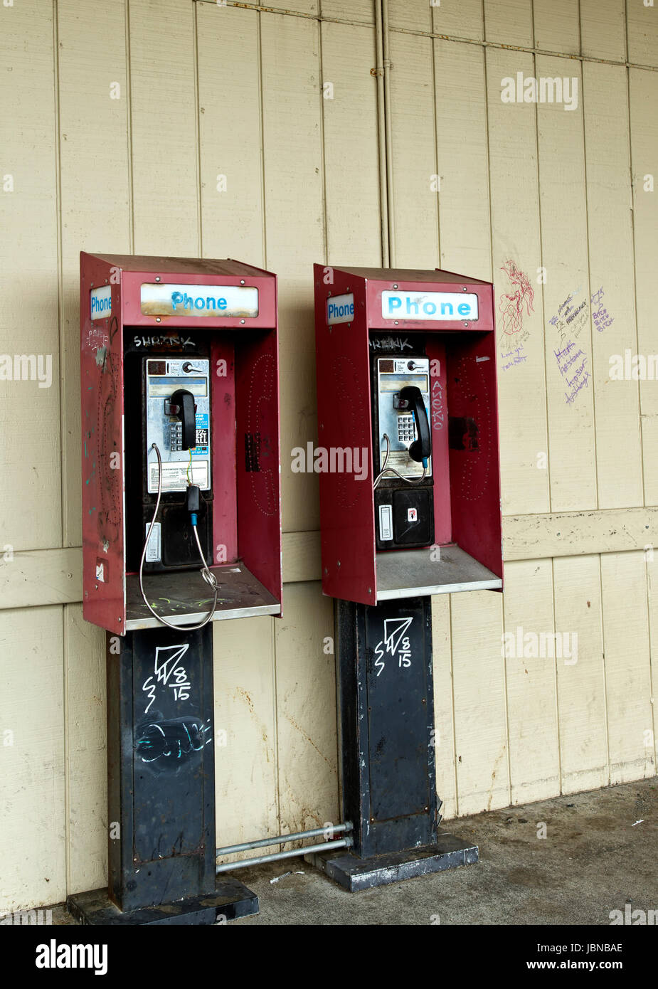 Abandoned coin operated public pay telephone with coin release slot,  graffiti on wall & telephones. Stock Photo