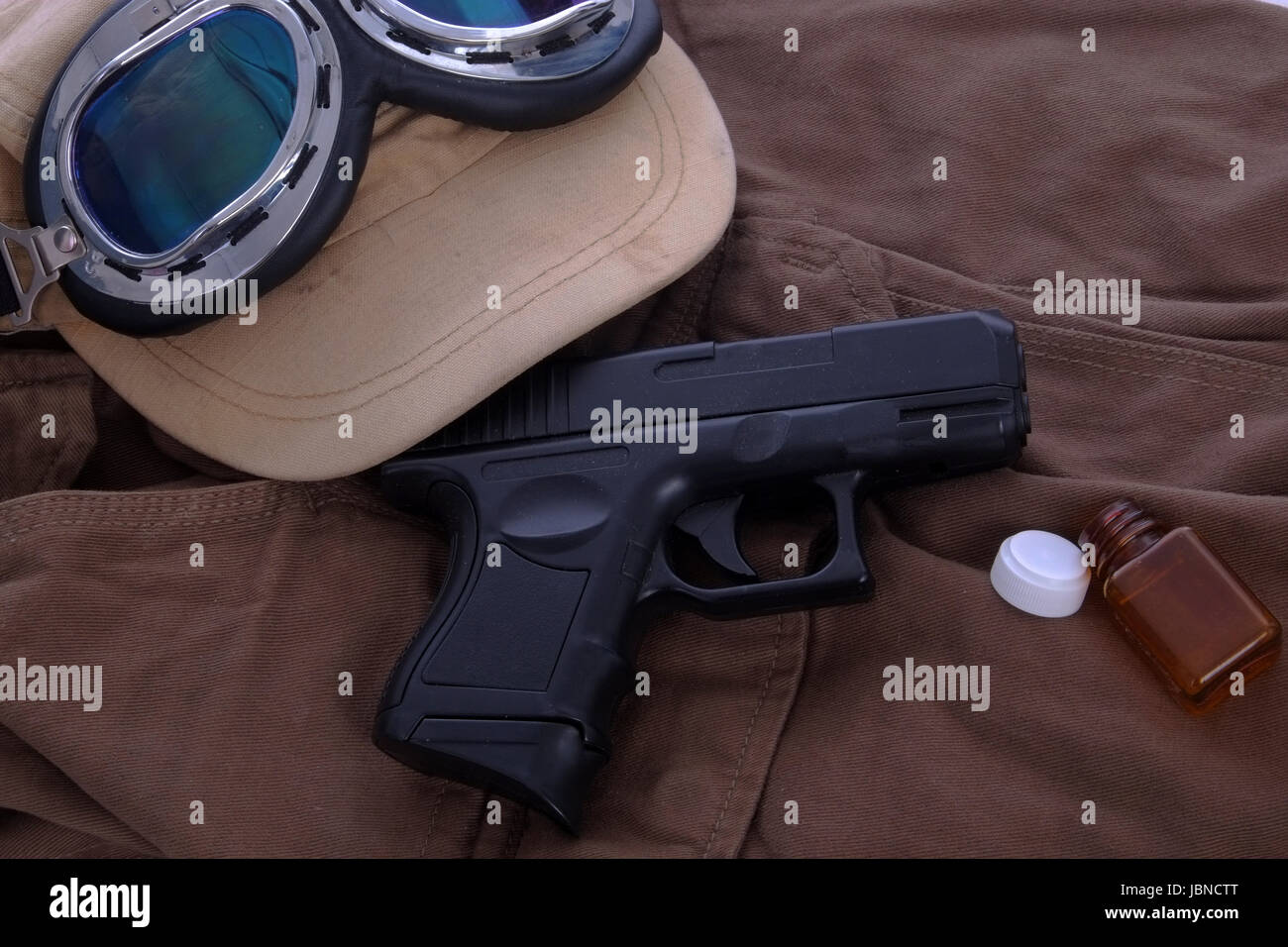 Science fiction or wartime / battle concept table top still life, of gun, hat, goggles and empty pill bottle Stock Photo