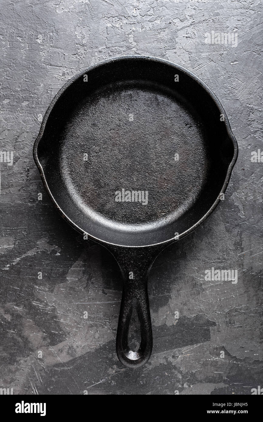 Empty cast iron frying pan on dark grey culinary background, view from