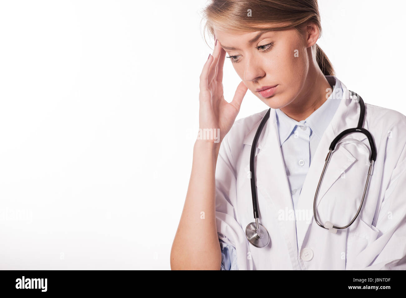Woman Nurse / doctor with migraine headache overworked and stressed. Health care professional in lab coat wearing stethoscope at hospital. Stock Photo