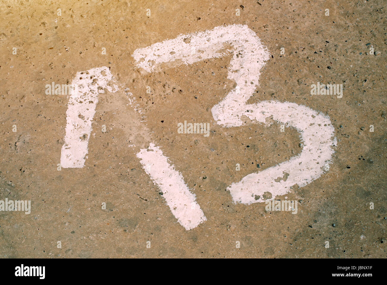 Number thirteen on the concrete floor, sign on empty private parking lot, 13 is considered to be unlucky number in many countries Stock Photo