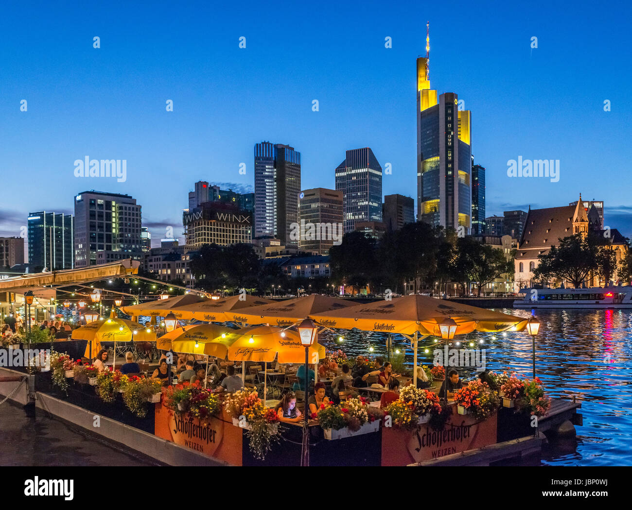 Frankfurt, Germany. Night view of Bootshaus floating restaurant onbanks of the River Main with financial district behind, Frankfurt, Hesse, Germany Stock Photo