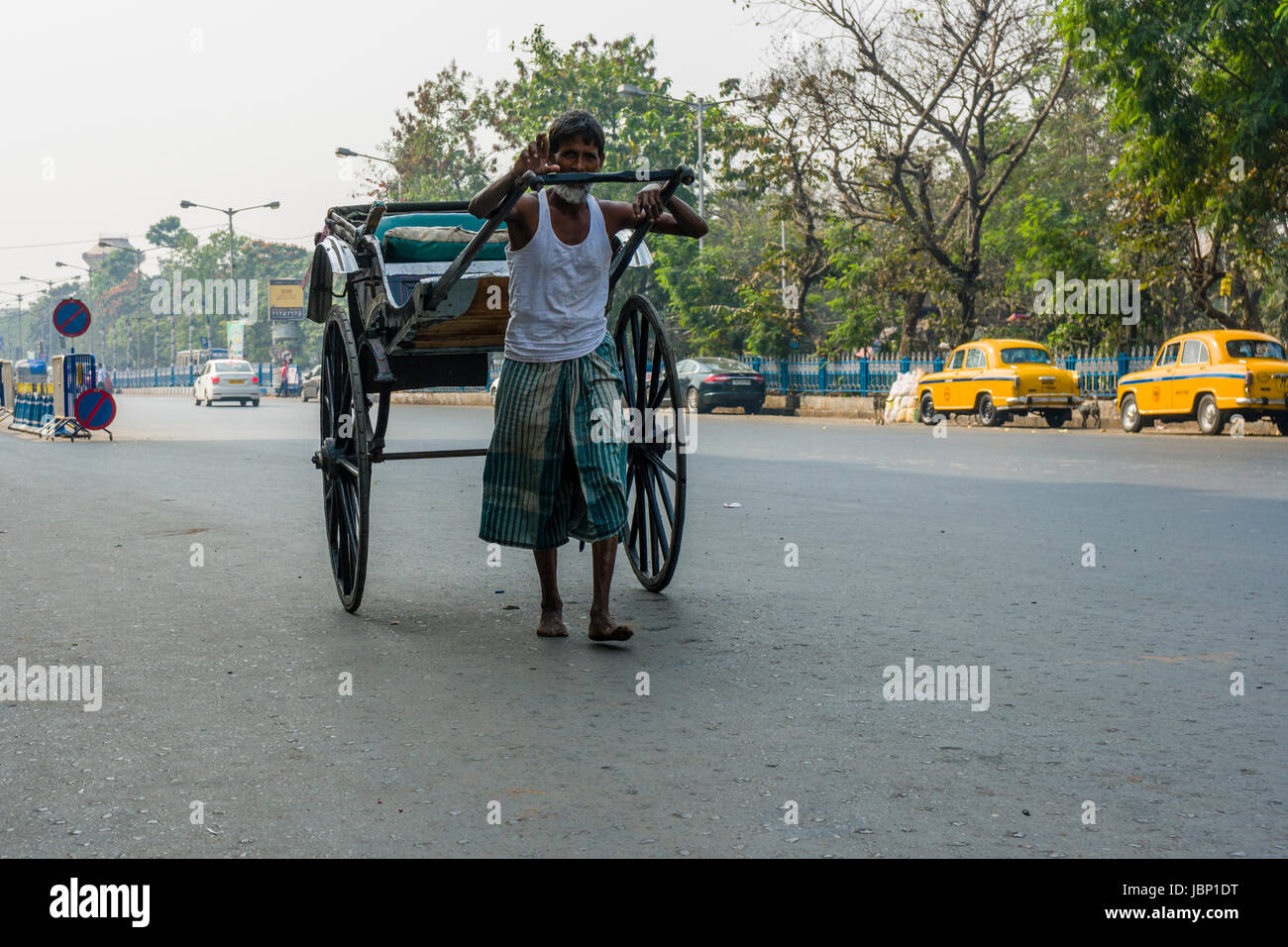 A man is pulling a rickshaw, looking for customers, on a road in the suburb Esplanade Stock Photo