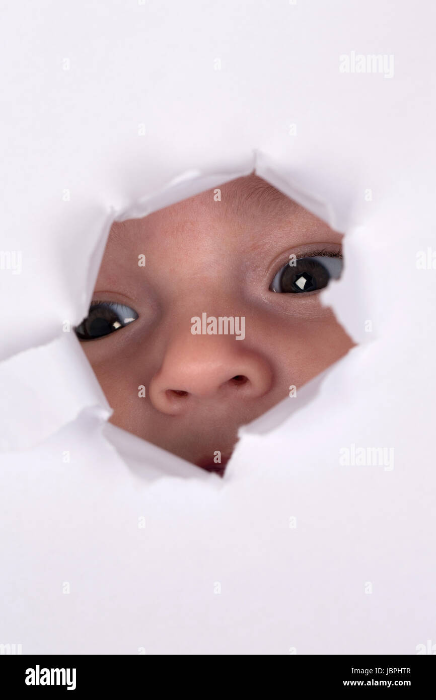 Kleines Baby schaut durch ein Loch, Thema Neugier mit Textfreiraum Stock Photo