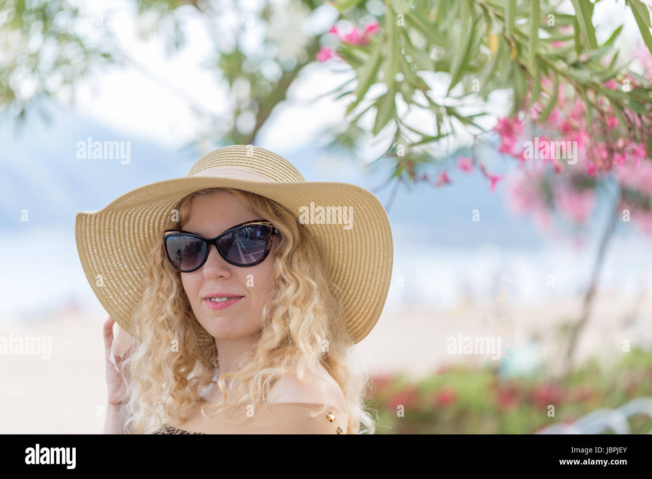 Beautiful blonde on the beach with hat and sunglasses in vacation among ...