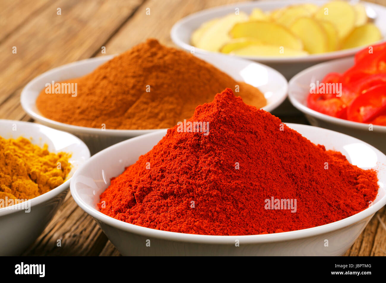 Bowls of curry powder, paprika,  ground cinnamon, sliced ginger root and red pepper Stock Photo
