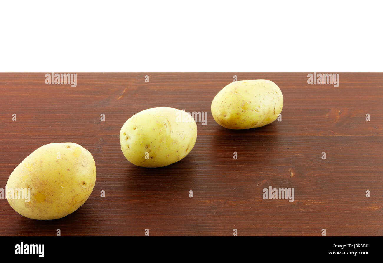 Drei Kartoffelknollen auf einem Holzbrett, mit weißem Hintergrund. Stock Photo