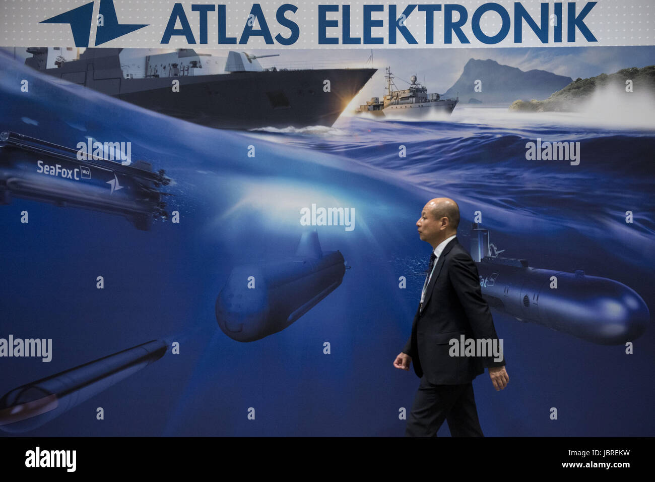 June 12, 2017 - Chiba, Chiba, Japan - A man passes in front of an image of Atlas Elektronik stand during the MAST Asia 2017 (Maritime Security between Asia-Pacific, Europe, and Americas) defense exhibition and conference in Chiba, Japan. According to its organisers, the biennial high technology defence industry fair, designed for the defence, security, maritime, air and space industries, is generally thought to be the biggest defence industry fair in the Asia. Regular participants at MAST events represent over 40 countries, from North America, South America, Western and Eastern Europe, Asia an Stock Photo