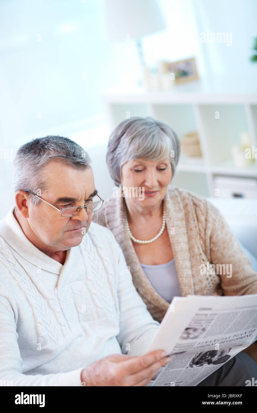 Image of couple of pensioners reading newspaper at home Stock Photo