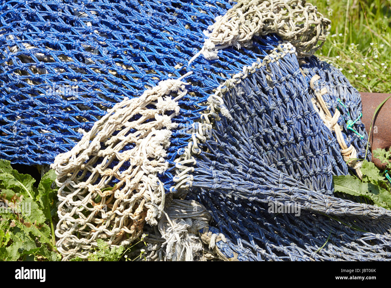 A pile of old fishing nets made of natural fibre and blue synthetic fiber are laying in the