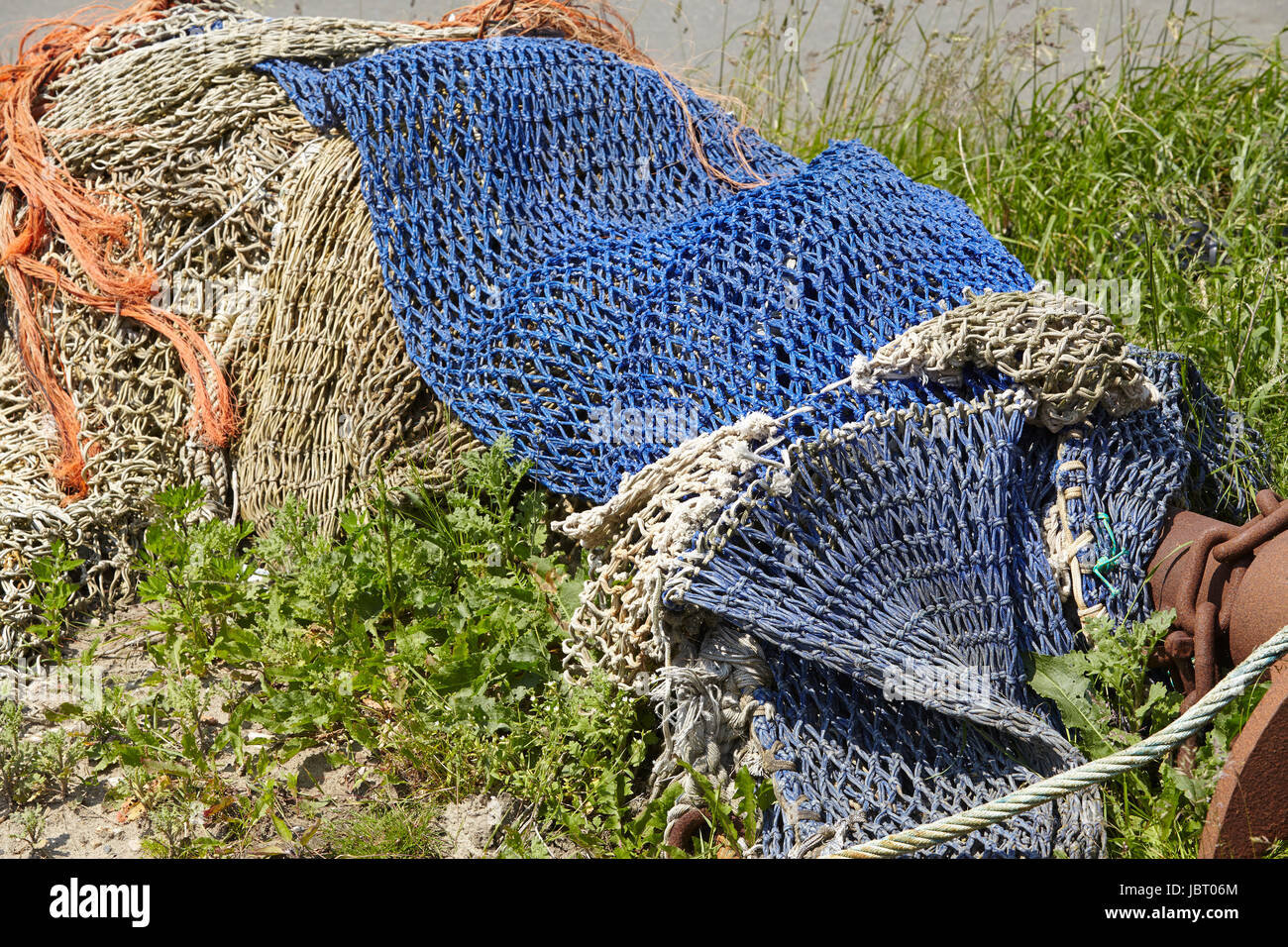 A pile of old fishing nets made of natural fibre and blue synthetic fiber are laying in the