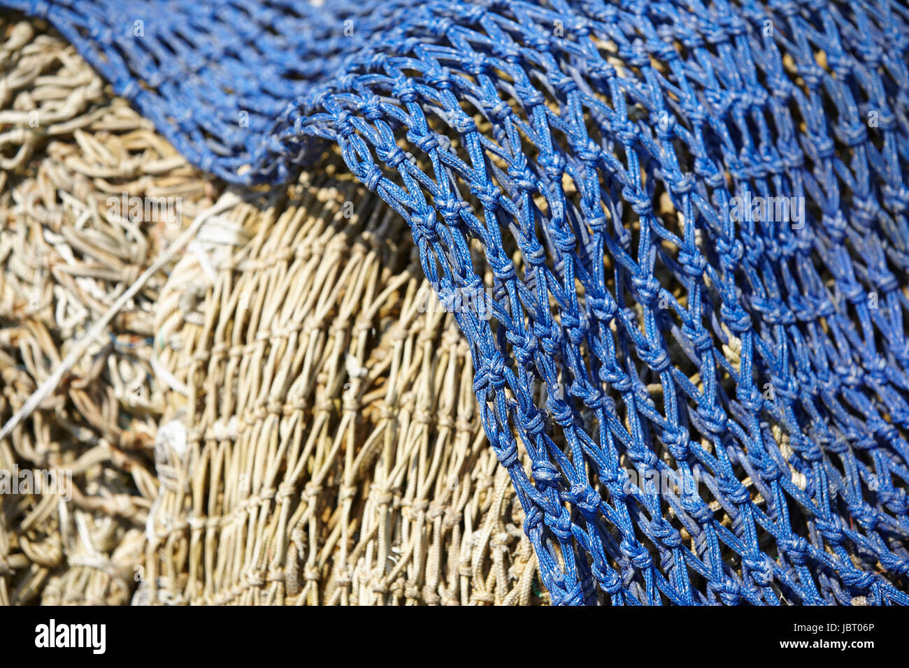 A pile of old fishing nets made of natural fibre and blue synthetic fiber are laying in the
