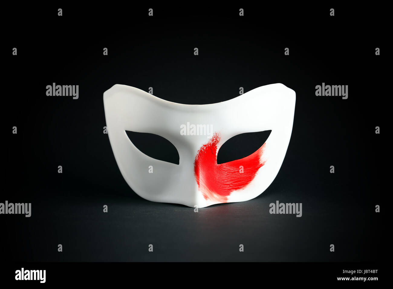 Art concept. White mask with red spot of paint on black background Stock Photo