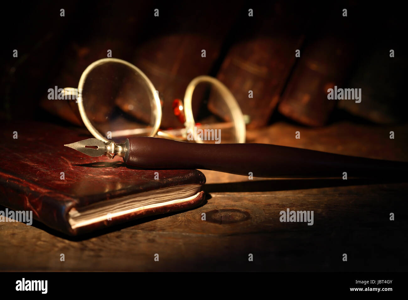 Vintage wooden pen on leather notebook near spectacles on background with old books Stock Photo