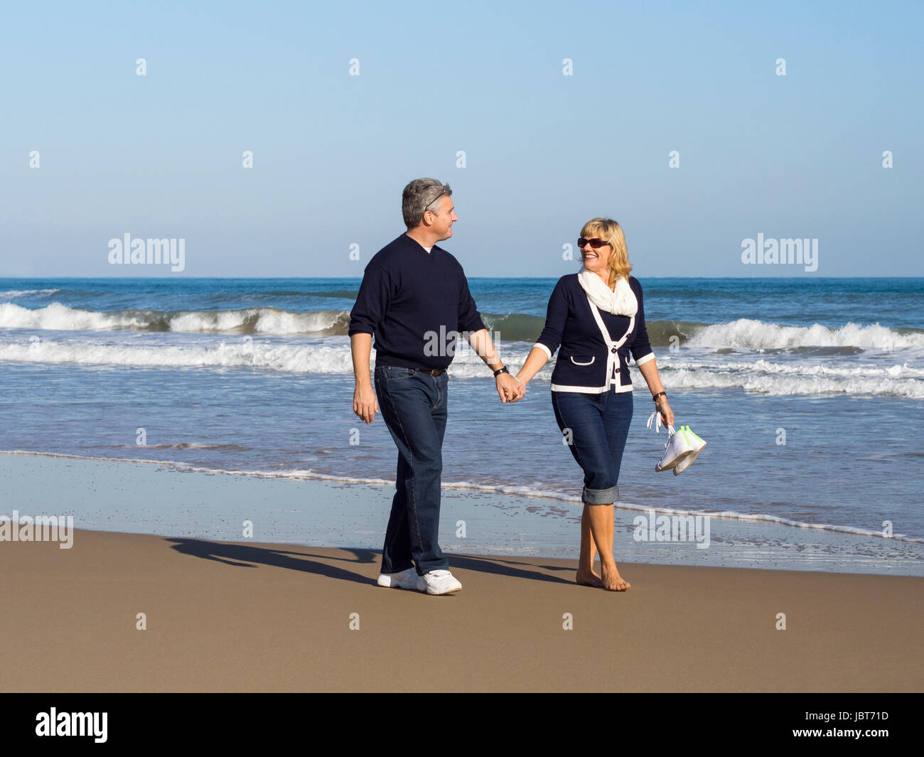 Attractive romantic mature couple walking along the beach hand in hand ...