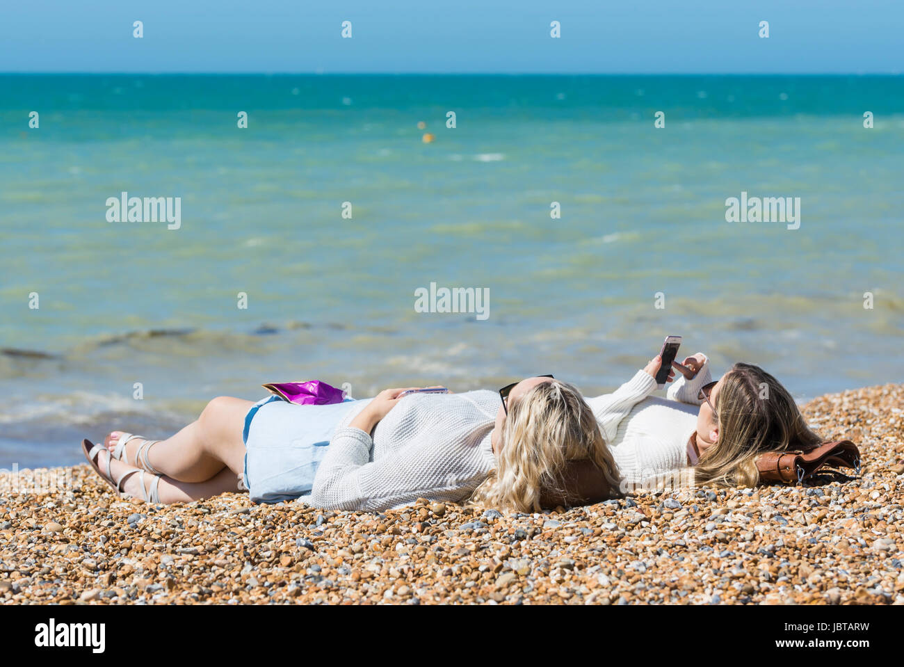 Female friends laying on their backs on a beach by the sea in Summer. Stock Photo