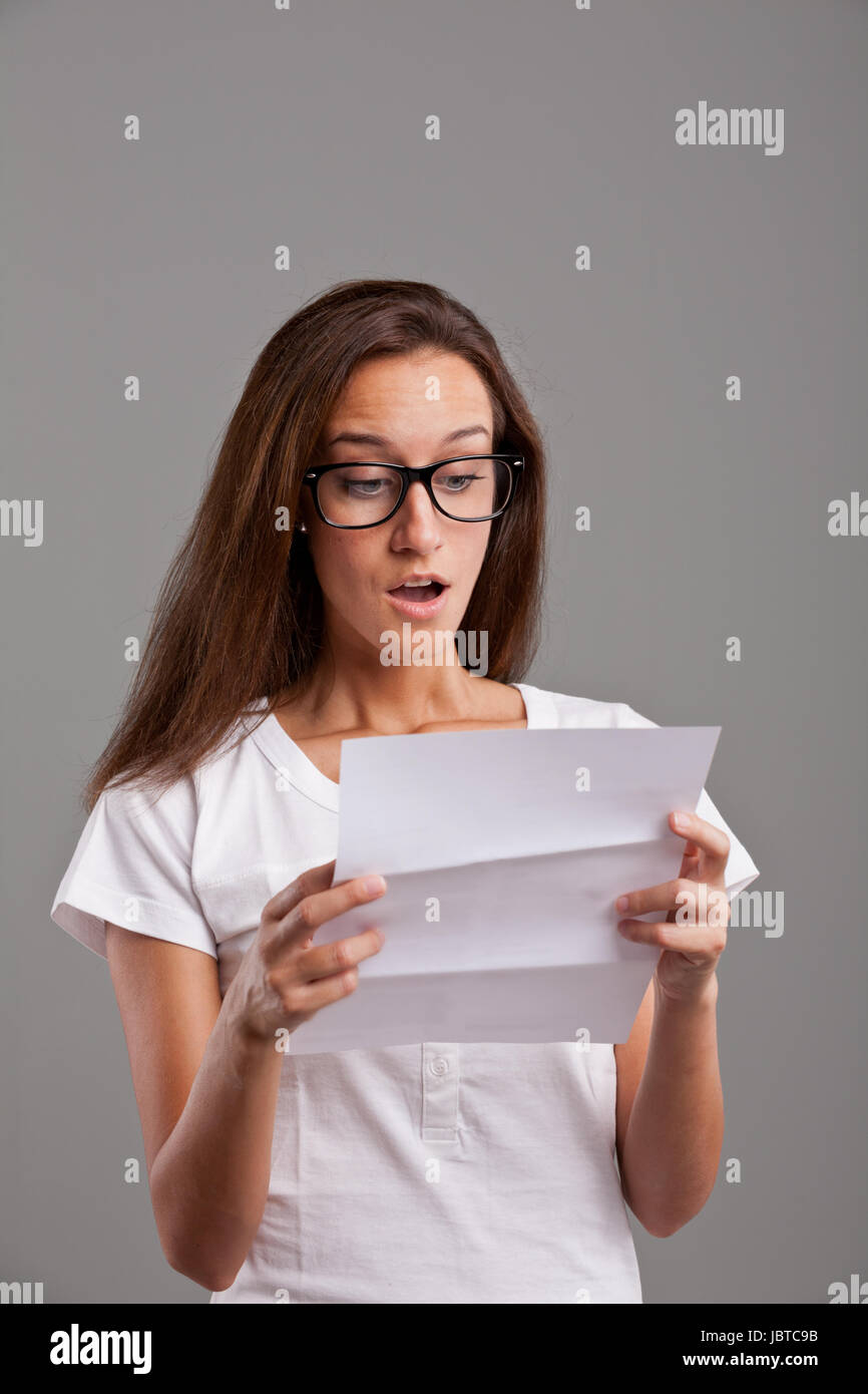 brunette young woman realizes that something amazing happened reading a white letter or document Stock Photo