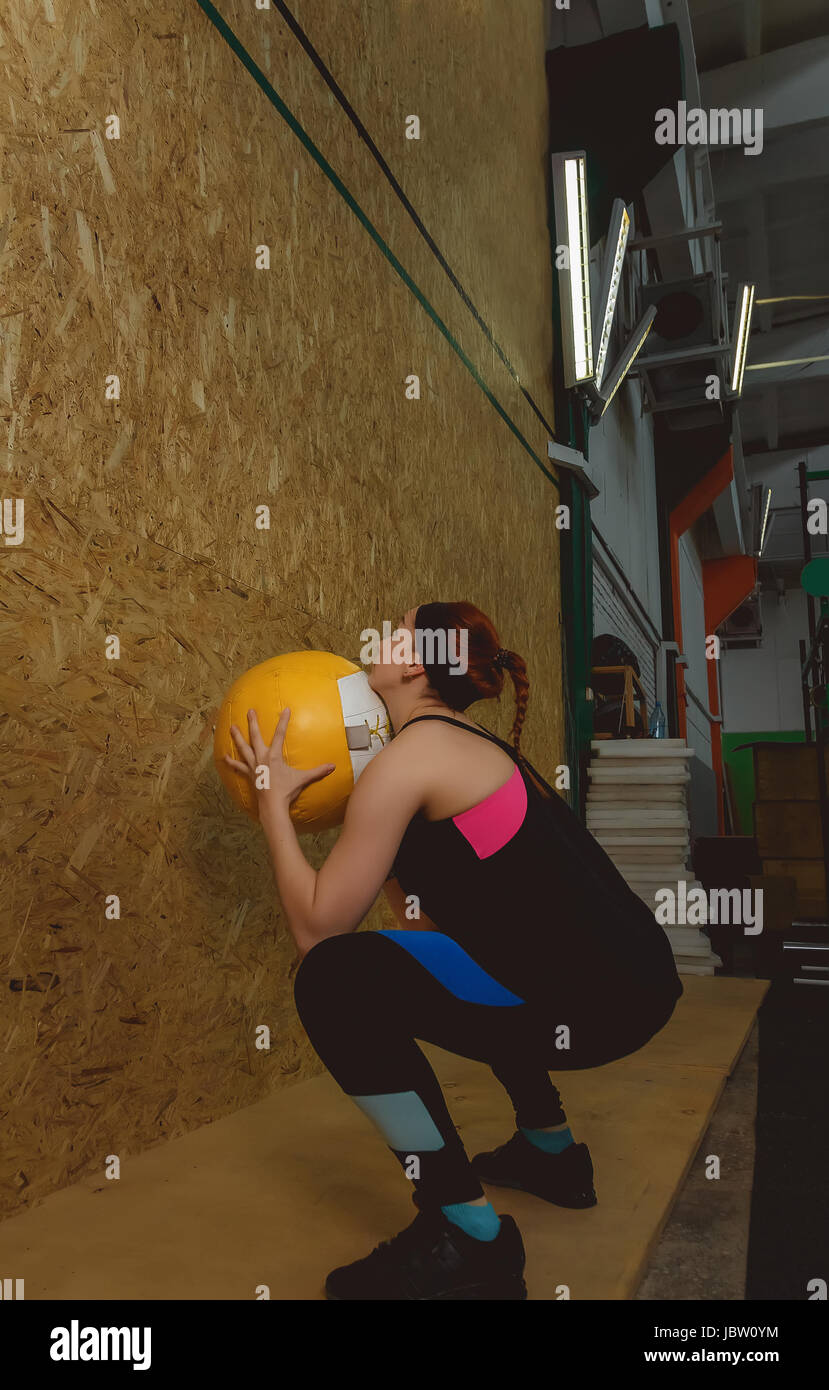 Young fit woman exercising by throwing a ball up in a gym Stock Photo